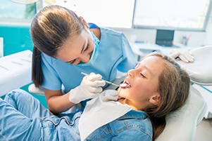 Young girl relaxes comfortably in a dental chair while a dentist inspects her teeth at Grins & Giggles Family Dentistry in Spokane Valley, WA