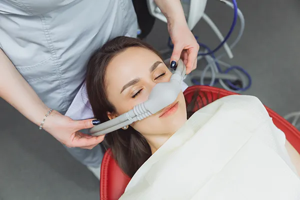 Dental assistant fitting a sedation mask over the nose of her calm female patient at Grins & Giggles Family Dentistry in Spokane Valley, WA