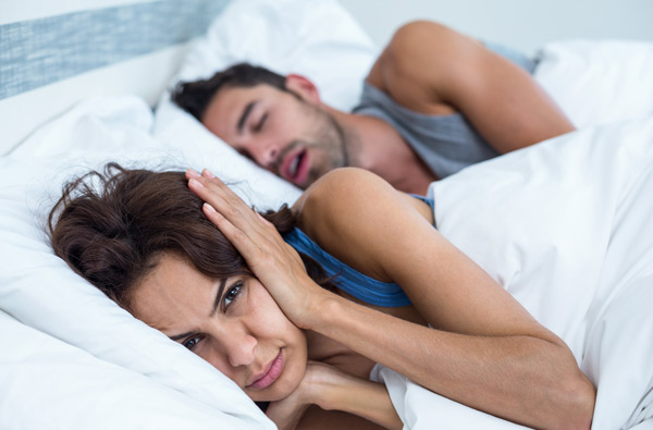 Woman covering ears while husband snores from sleep apnea before treatment at Grins & Giggles Family Dentistry in Spokane Valley, WA