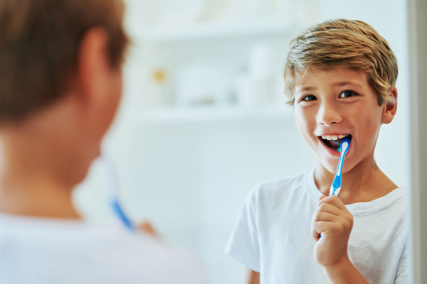 Young boy looking at mirror and brushing his teeth after learning brushing and flossing tips from Grins and Giggles Family Dentistry in Spokane Valley, WA
